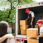 Asian,And,Caucasian,Workers,In,Uniform,Unloading,Cardboard,Boxes,From